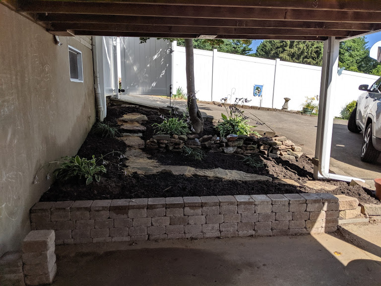 stone retaining wall behind house with plants, mulch, and decorative stone path